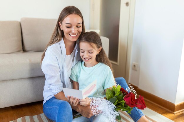 Eu amo minha mãe, uma jovem atraente com uma garotinha bonita está passando um tempo juntos em casa agradecendo pelo cartão artesanal com símbolo de amor e flores Conceito de família feliz Dia das mães