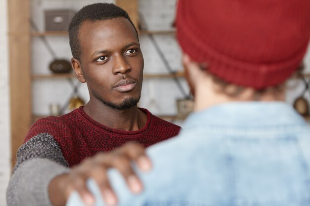 Eu estou sempre aqui para você. Foto interior de jovem afro-americano de coração caloroso, mostrando compaixão pelo homem irreconhecível, dando-lhe um tapinha no ombro enquanto tenta confortar e tranquilizar seu melhor amigo