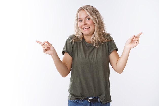 Eu não sei, decida você mesmo. Mulher loira atraente incerta e sem noção em uma camiseta verde-oliva encolhendo os ombros inconsciente, apontando para a esquerda e para a direita em direções diferentes perguntando qual escolha escolher