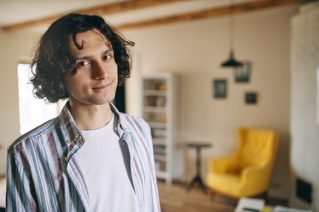 Foto grátis europeu jovem bonito morando sozinho, passando o dia todo em casa enquanto se distanciava socialmente, sendo otimista e despreocupado, olhando para a câmera com um sorriso