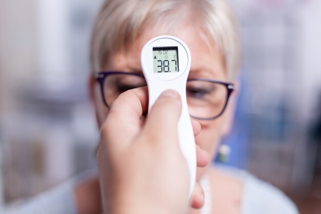 Exame da temperatura corporal da mulher idosa em quarto de hospital durante o teste de exame