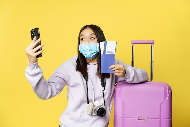 Excitada garota turística asiática viajando tomando selfie em smartphone com passagens aéreas e passaporte g ...