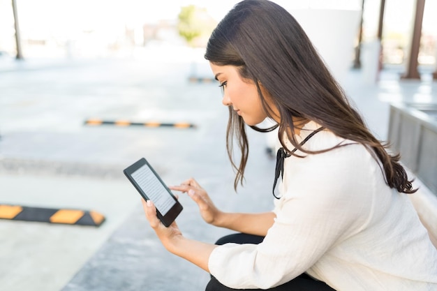 Executivo atraente com longos cabelos castanhos segurando o e-reader no estacionamento