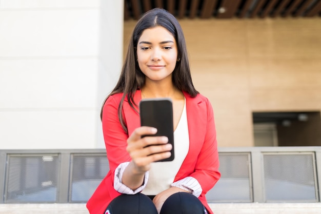 Executivo feminino bonito lendo a notificação recebida no smartphone enquanto está sentado fora do escritório