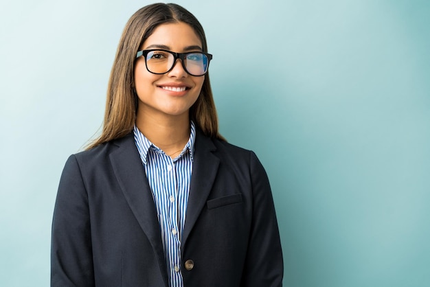 Executivo feminino hispânico sorridente usando óculos em pé no estúdio
