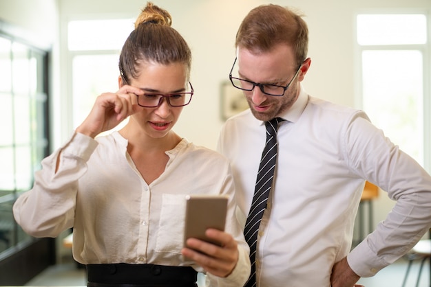 Executivos focalizados que leem notícias no smartphone.