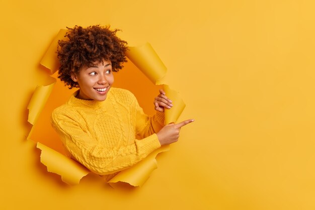 Experimente isso! Jovem afro-americana de aparência agradável e alegre aponta para o espaço em branco da cópia