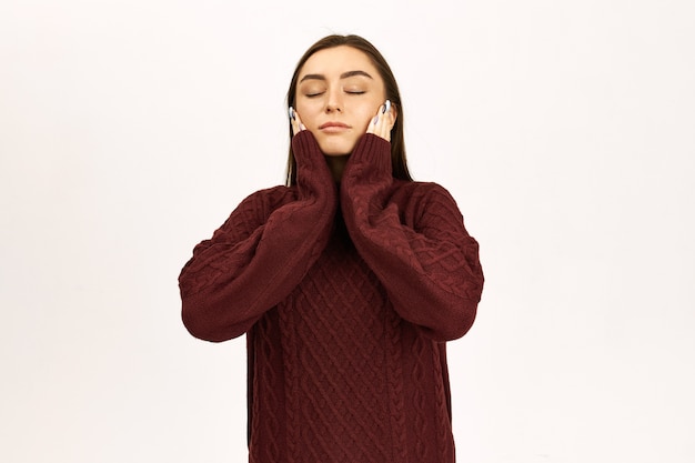 Expressões faciais humanas e linguagem corporal. Imagem de estúdio de uma mulher europeia jovem e atraente fechando os olhos, segurando as mãos nas bochechas, sonhando, meditando ou tirando uma soneca, vestindo um macacão