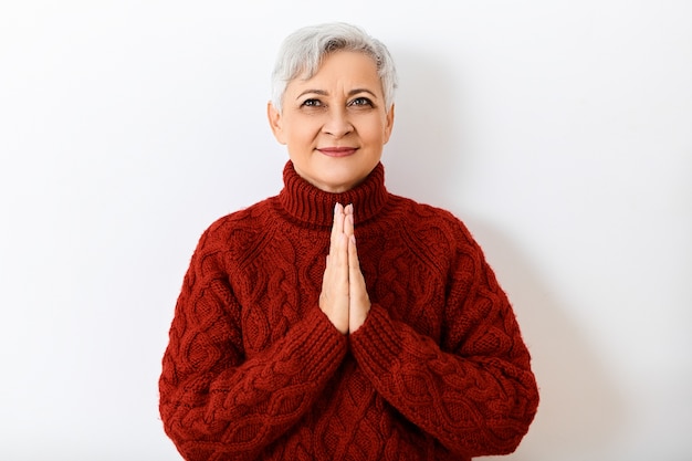 Expressões faciais humanas, emoções, sentimentos e reações. Imagem isolada de uma mulher aposentada alegre positiva com cabelo curto, olhando para cima com um sorriso feliz, de mãos dadas em oração, com olhar esperançoso