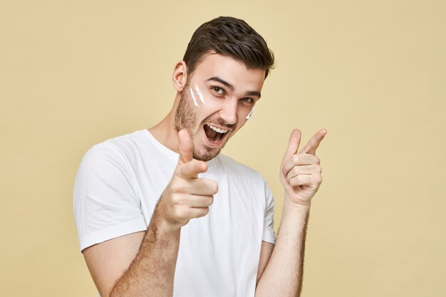 Expressões faciais humanas positivas, emoções e linguagem corporal. Retrato de um jovem homem barbado e bonito e muito feliz com espuma nas bochechas, exclamando com entusiasmo e apontando os dedos da frente