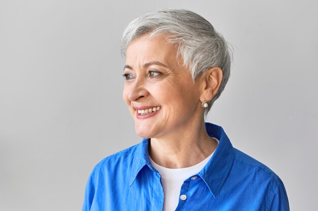 Expressões faciais humanas positivas, emoções, sentimentos e reações. Perfil de uma mulher europeia bonita e elegante, vestindo camisa azul e penteado de duende estiloso, rindo de uma boa piada engraçada