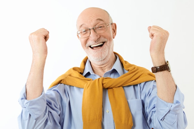 Foto grátis expressões faciais, sentimentos e reações humanas genuínas. homem aposentado elegante e bonito, de óculos e camisa, com olhar radiante de êxtase, punhos cerrados e entusiasmado com o sucesso ou boas notícias