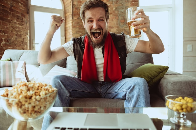 Foto grátis fã de futebol animado assistindo jogo de esporte em casa, suporte remoto do time favorito durante surto de pandemia de coronavírus