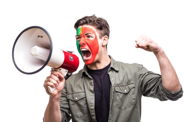 Fã leal de torcedor homem bonito da seleção nacional de portugal pintou o rosto da bandeira obter vitória feliz gritando no megafone com a mão pontuda. emoções dos fãs.