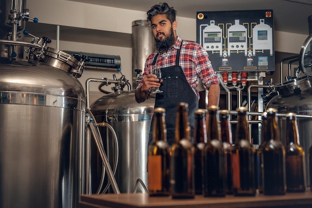 Fabricante masculino hipster tatuado e barbudo indiano apresentando cerveja artesanal na microcervejaria.