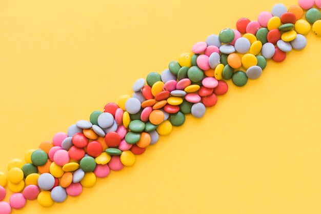 Faixas coloridas de doces de pedras preciosas em fundo amarelo