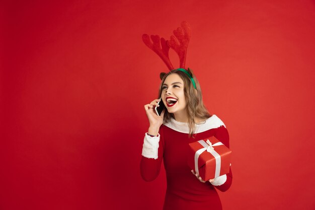 Falando telefone com presente. Conceito de Natal, Ano Novo, clima de inverno, feriados. Linda mulher caucasiana com cabelo comprido como a caixa de presente pegando renas do Papai Noel.