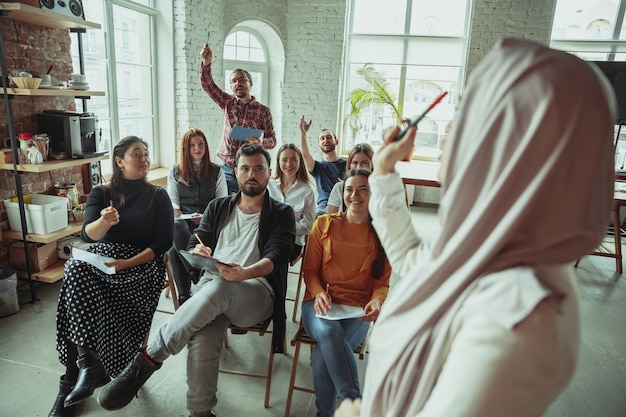 Falante muçulmana feminina, fazendo uma apresentação no corredor do workshop. Audiência ou sala de conferências. Perguntar aos participantes na audiência. Evento de conferência, treinamento. Educação, diversidade, conceito inclusivo.