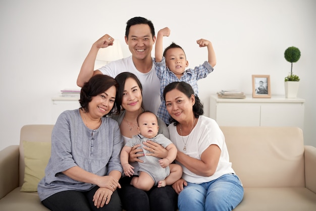 Família asiática extensa com bebê e criança posando juntos em torno do sofá em casa