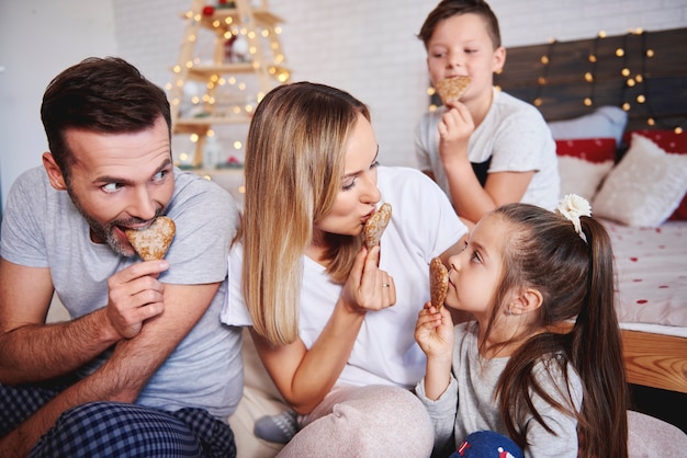 Família brincalhona comendo biscoitos de gengibre na cama