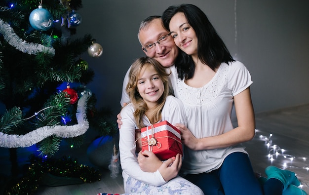 Família com caixa de presente na árvore de natal