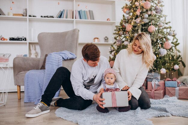 Família com filha pequena desembalar presentes pela árvore de Natal