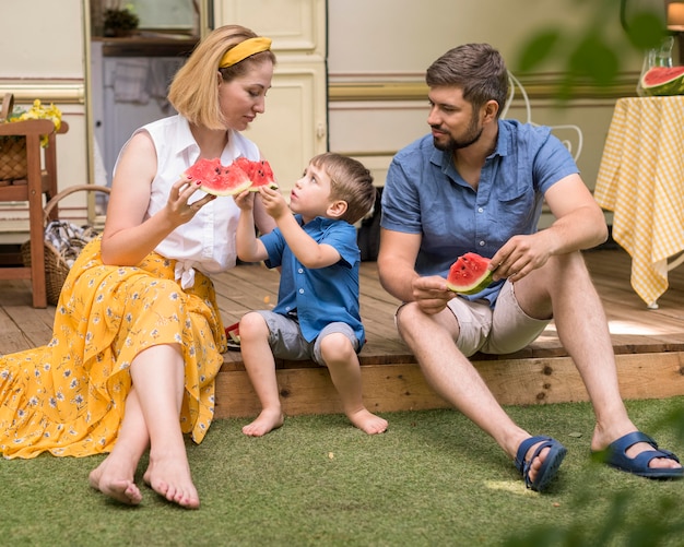 Família comendo melancia junta ao lado de uma caravana