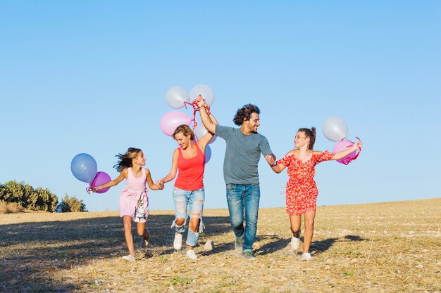 Família correndo no campo e segurando balões