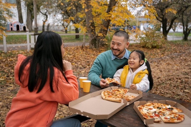 Família de tiro médio comendo pizza ao ar livre