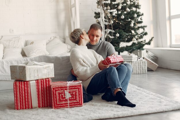 Família em casa. Casal perto de decorações de Natal. Mulher com um suéter cinza.