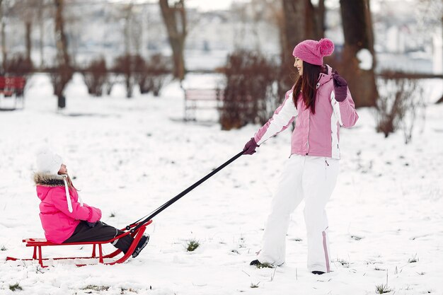 Família em chapéus de malha de inverno nas férias de Natal em família. Mulher e menina em um parque. Pessoas brincando com trenó.