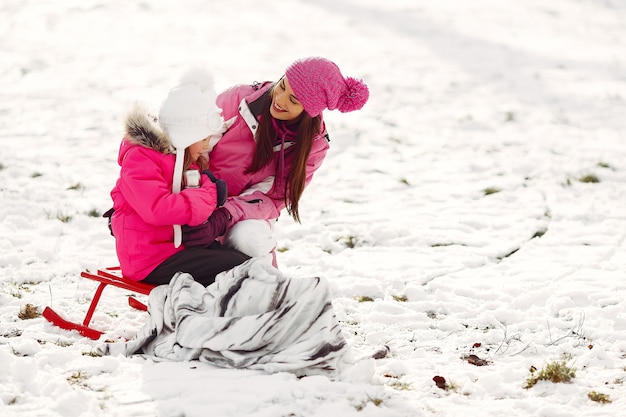 Família em chapéus de malha de inverno nas férias de Natal em família. Mulher e menina em um parque. Pessoas com garrafa térmica.