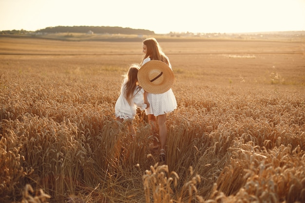 Família em um campo de trigo. Mulher de vestido branco. Menina com chapéu de palha.