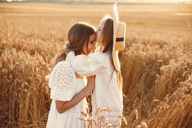 Família em um campo de trigo. Mulher de vestido branco. Menina com chapéu de palha.