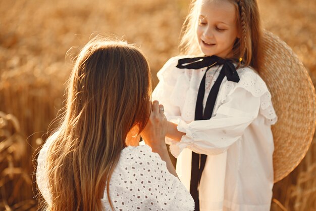 Família em um campo de trigo. Mulher de vestido branco. Menina com chapéu de palha.