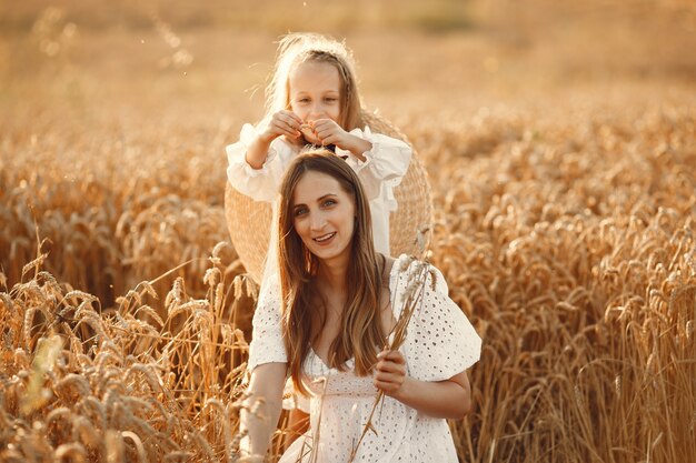 Família em um campo de trigo. Mulher de vestido branco. Menina com chapéu de palha.