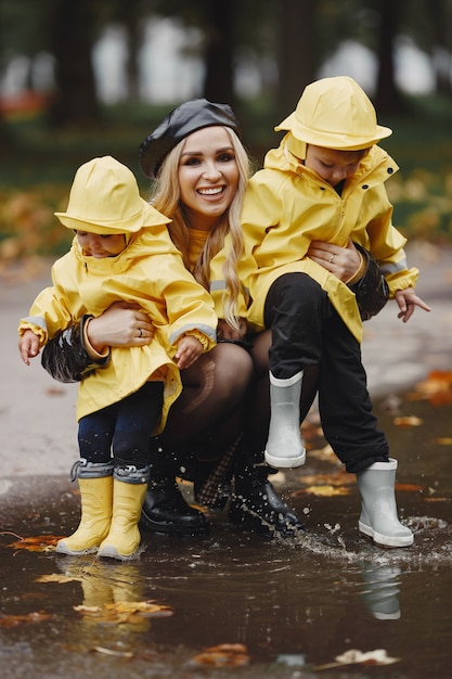Família em um parque chuvoso. Crianças com capas de chuva. Mãe com filho. Mulher com um casaco preto.