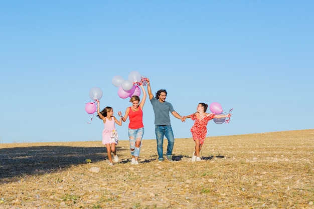 Família feliz caminhando no campo com balões