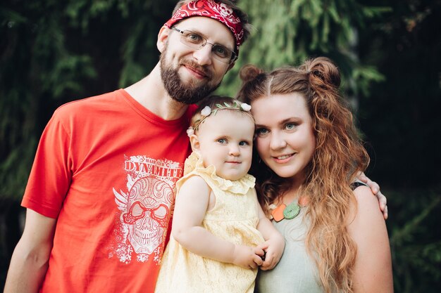 Família feliz com menina rindo posando juntos ao ar livre no fundo da árvore verde. mãe e pai sorridentes segurando crianças aproveitando a paternidade