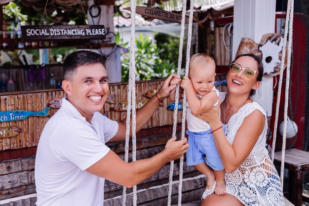 Família feliz com um bebê em um balanço do lado de fora do hotel