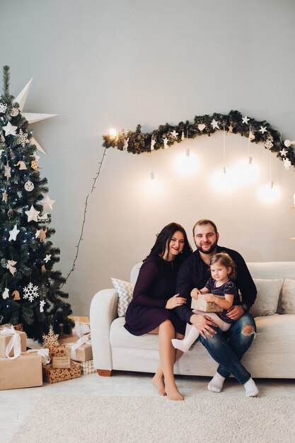 Família feliz com uma criança senta no sofá ao lado da árvore de Natal e relaxa