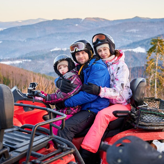 Família feliz de três passando ótimos momentos juntos nas montanhas no inverno andando de quadriciclo