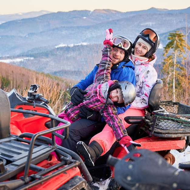 Família feliz de três passando ótimos momentos juntos nas montanhas no inverno andando de quadriciclo