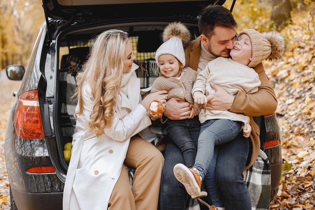 Família feliz descansando após o dia passar ao ar livre no parque outono. Pai, mãe e dois filhos sentados no porta-malas do carro, sorrindo. Férias em família e conceito de viagem.