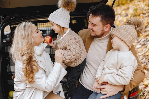 Família feliz descansando após o dia passar ao ar livre no parque outono. Pai, mãe e dois filhos sentados no porta-malas do carro, sorrindo. Férias em família e conceito de viagem.