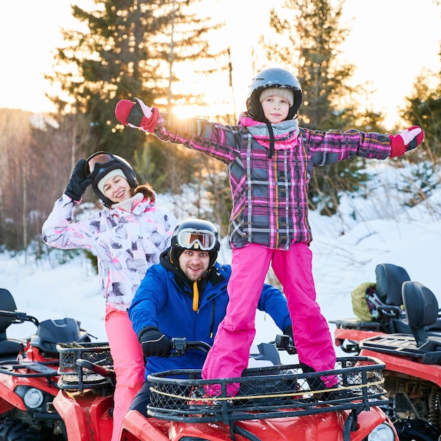Família feliz dirigindo moto-quatro nas montanhas de inverno