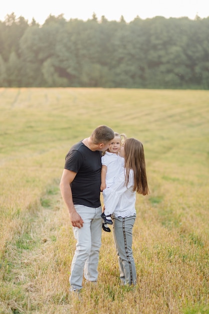 Família feliz em um campo no outono. Mãe, pai e bebê brincam na natureza sob os raios do pôr do sol