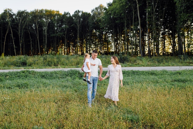 Família feliz em um parque no outono de verão. Mãe, pai e bebê brincam na natureza sob os raios do pôr do sol