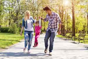 Foto grátis família feliz, jovens pais caucasianos caminhando com a filha em um parque