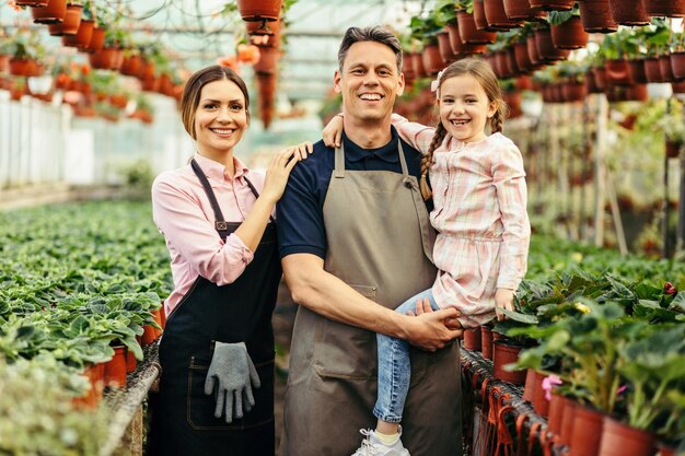 Família feliz juntos no viveiro de plantas e olhando para a câmera